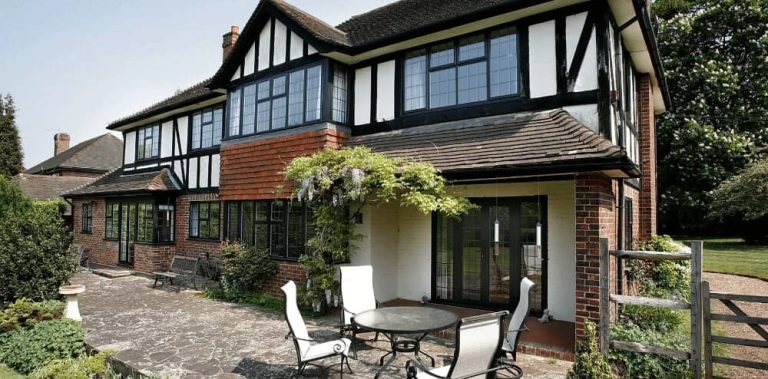 Traditional black-and-white Tudor-style house with modern aluminium windows and patio doors opening onto a garden seating area.