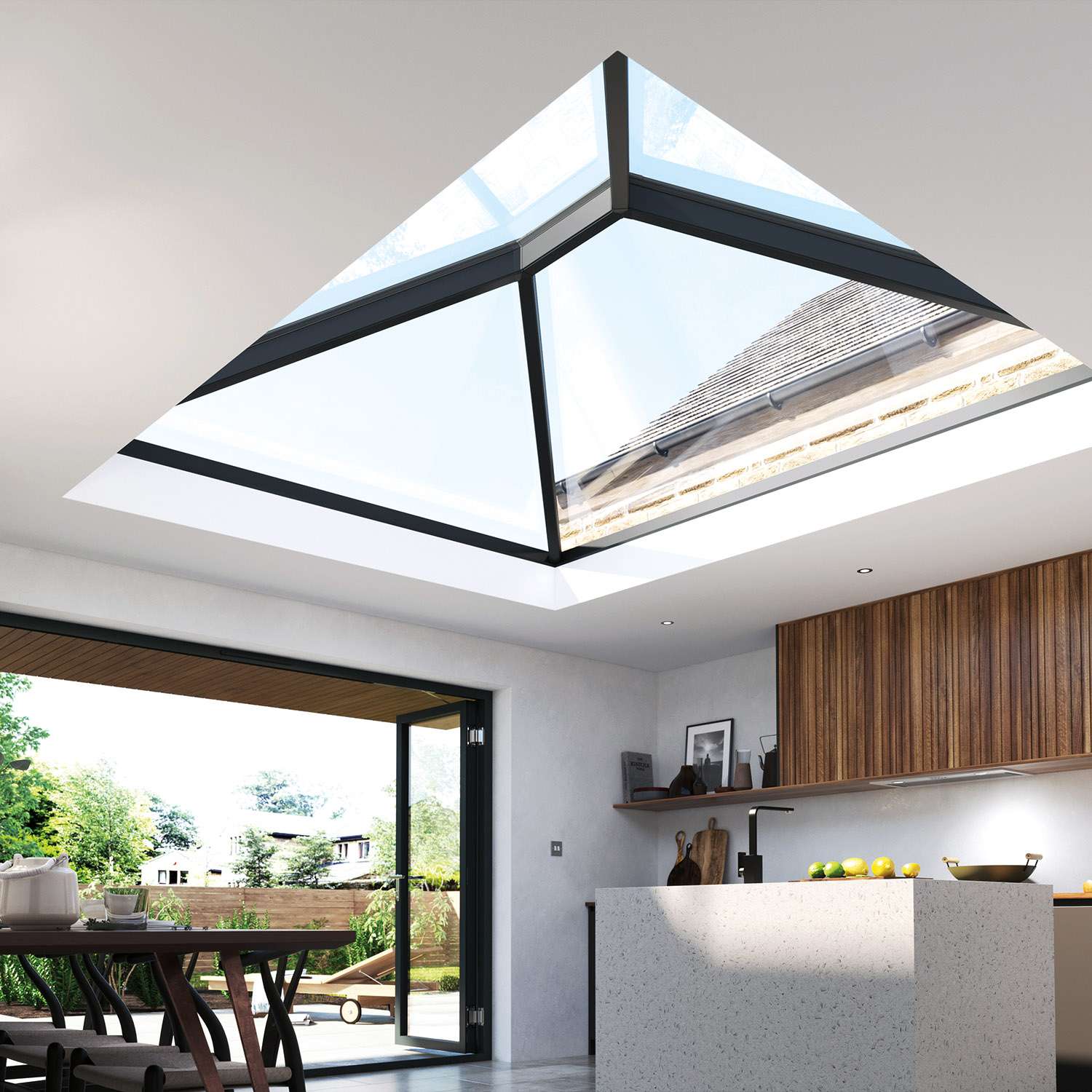 A modern kitchen featuring a Korniche Roof Lantern, which is a large, pyramid-shaped glass structure integrated into the ceiling, allowing natural light to flood the space. The kitchen has a minimalist design with sleek, wooden cabinetry, a white countertop island, and an open dining area that seamlessly extends to an outdoor patio through large, bi-fold glass doors. The scene is bright and airy, with a view of greenery outside.